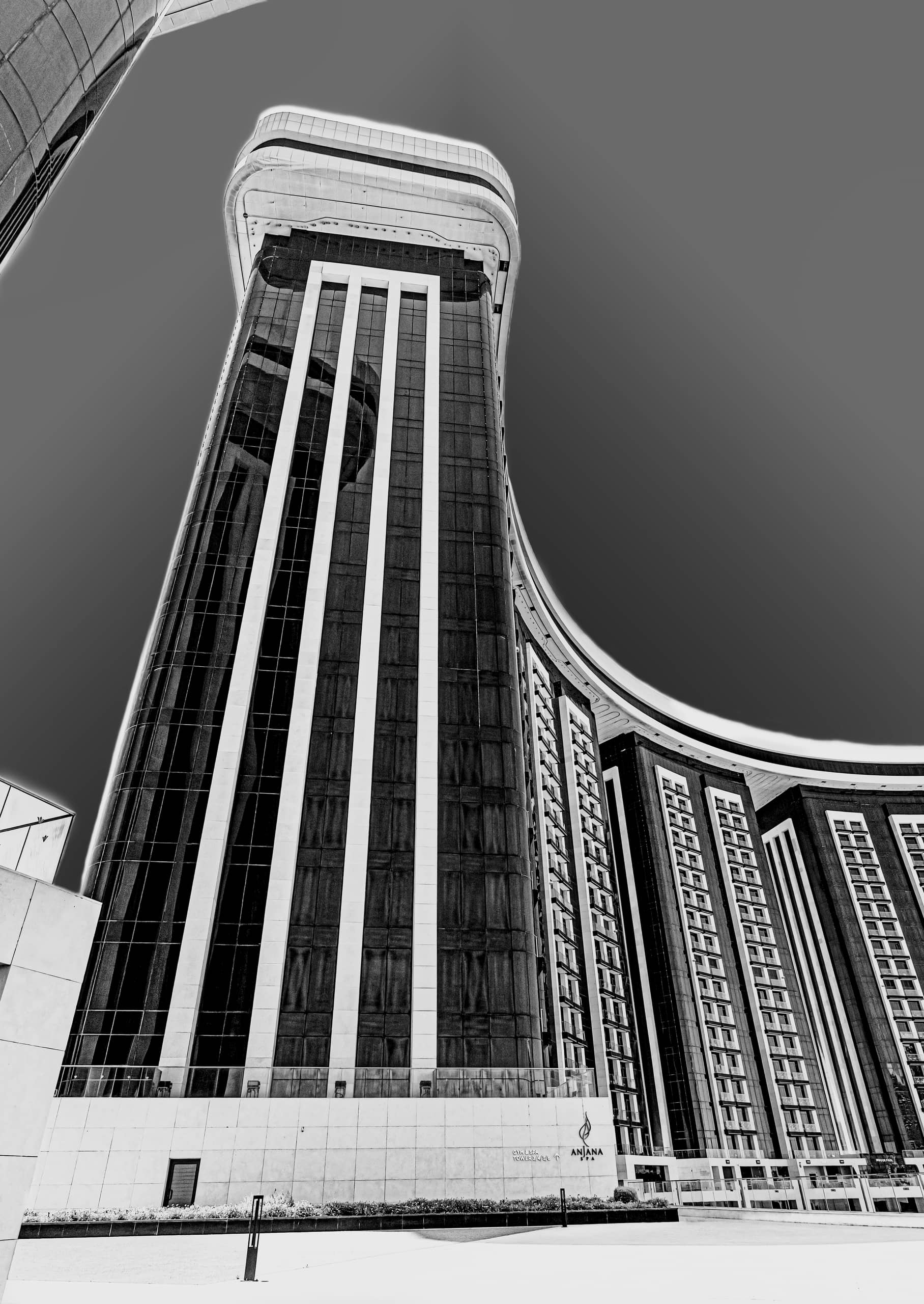 A black-and-white low-angle photograph of a curved modern high-rise building with dark glass panels and vertical white framing against a clear sky.