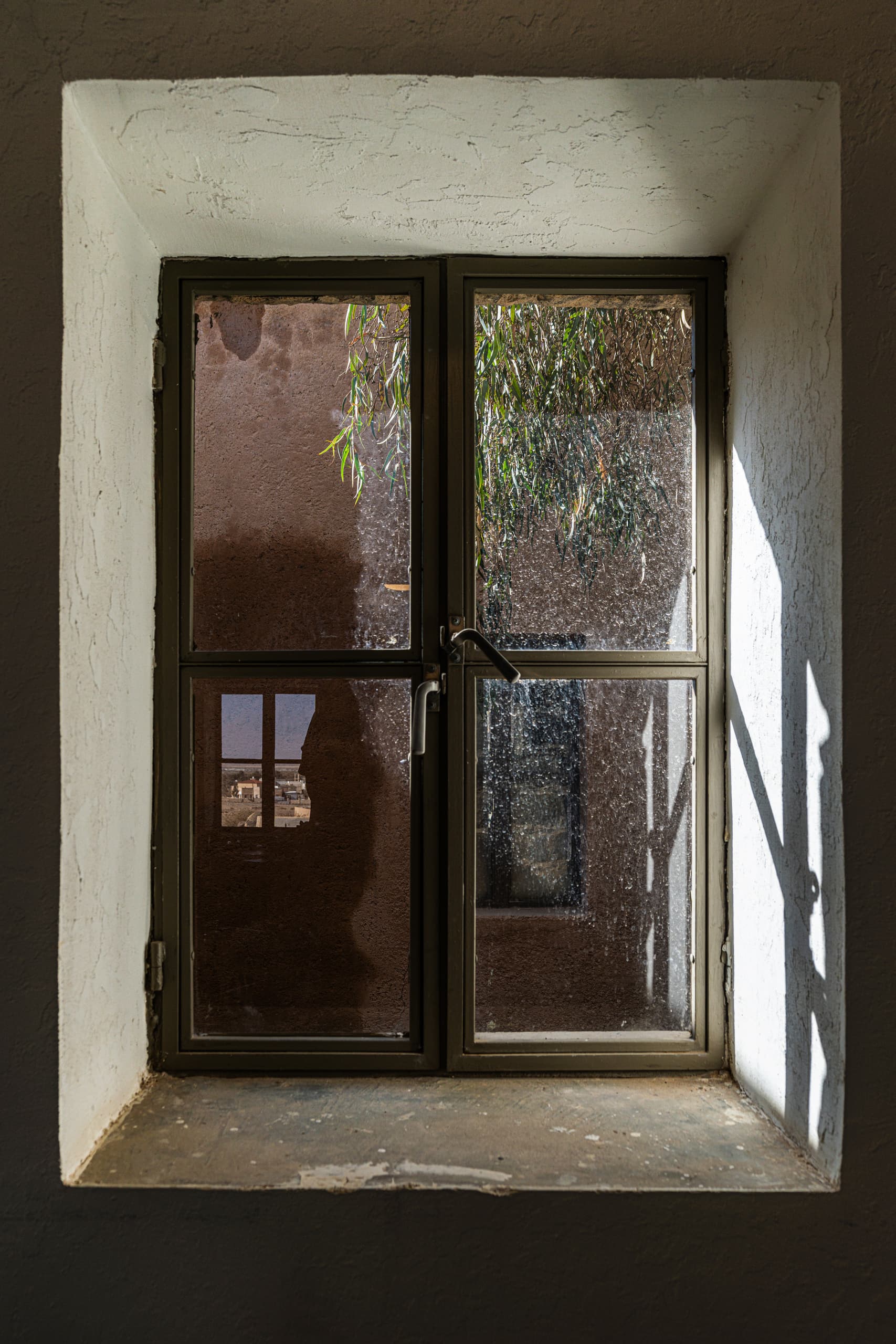 Interior view of a double-paned window set inside a thick white plaster wall with angled sunlight casting shadows on the right reveal.