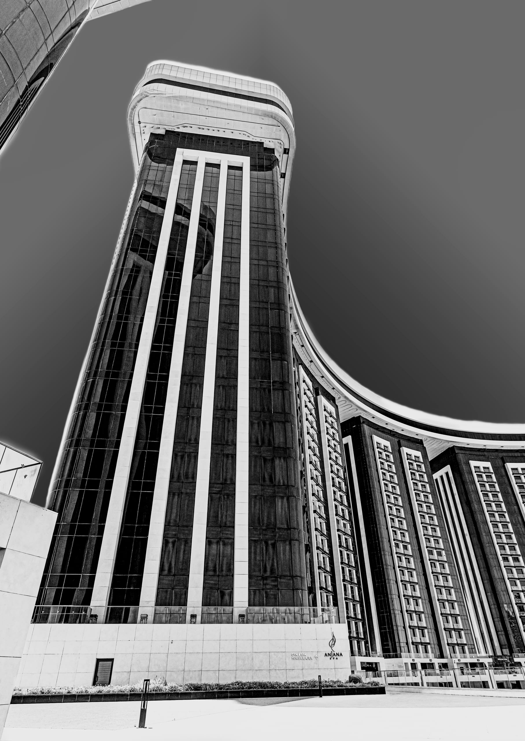 A black-and-white low-angle photograph of a curved modern high-rise building with dark glass panels and vertical white framing against a clear sky.