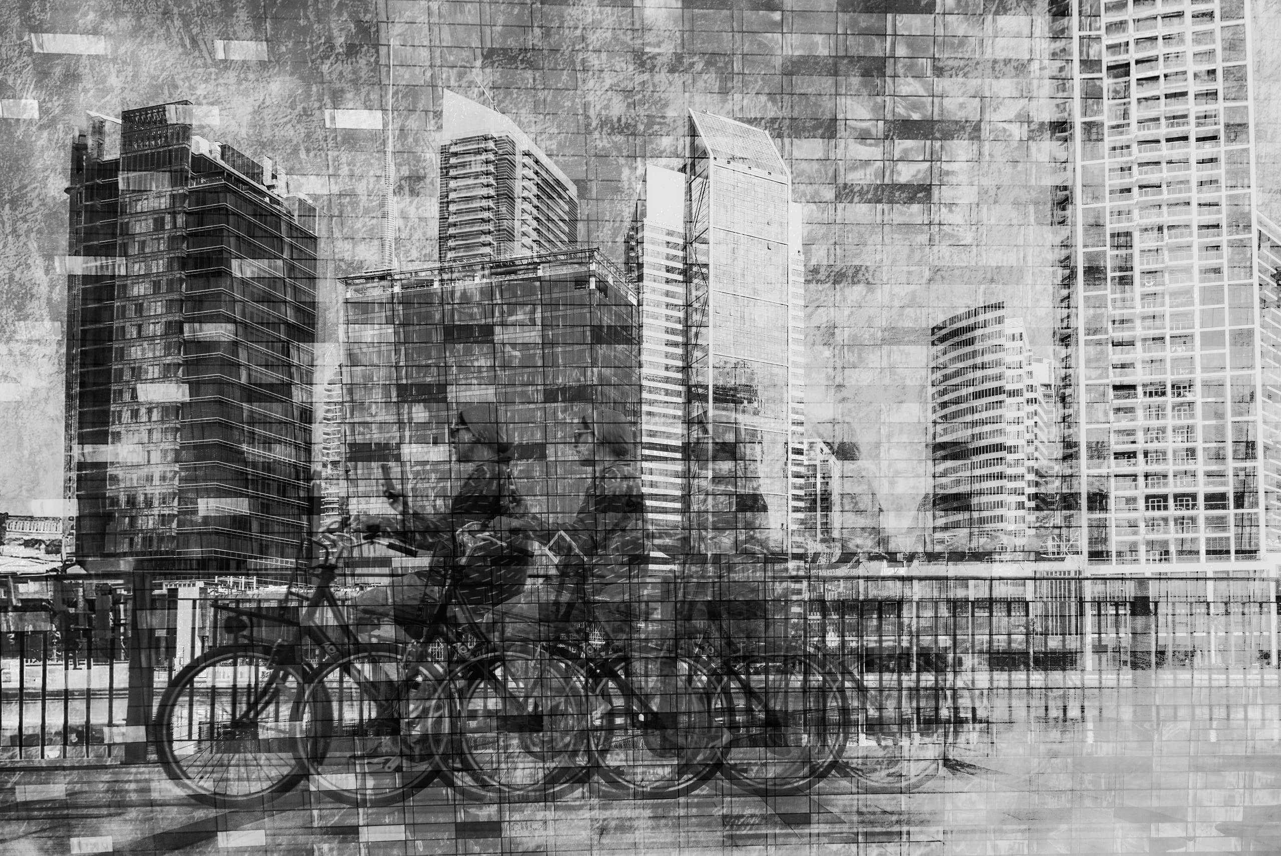 A black-and-white multiple exposure photograph showing a cyclist in motion against a backdrop of towering high-rise buildings and overlapping architectural grids.