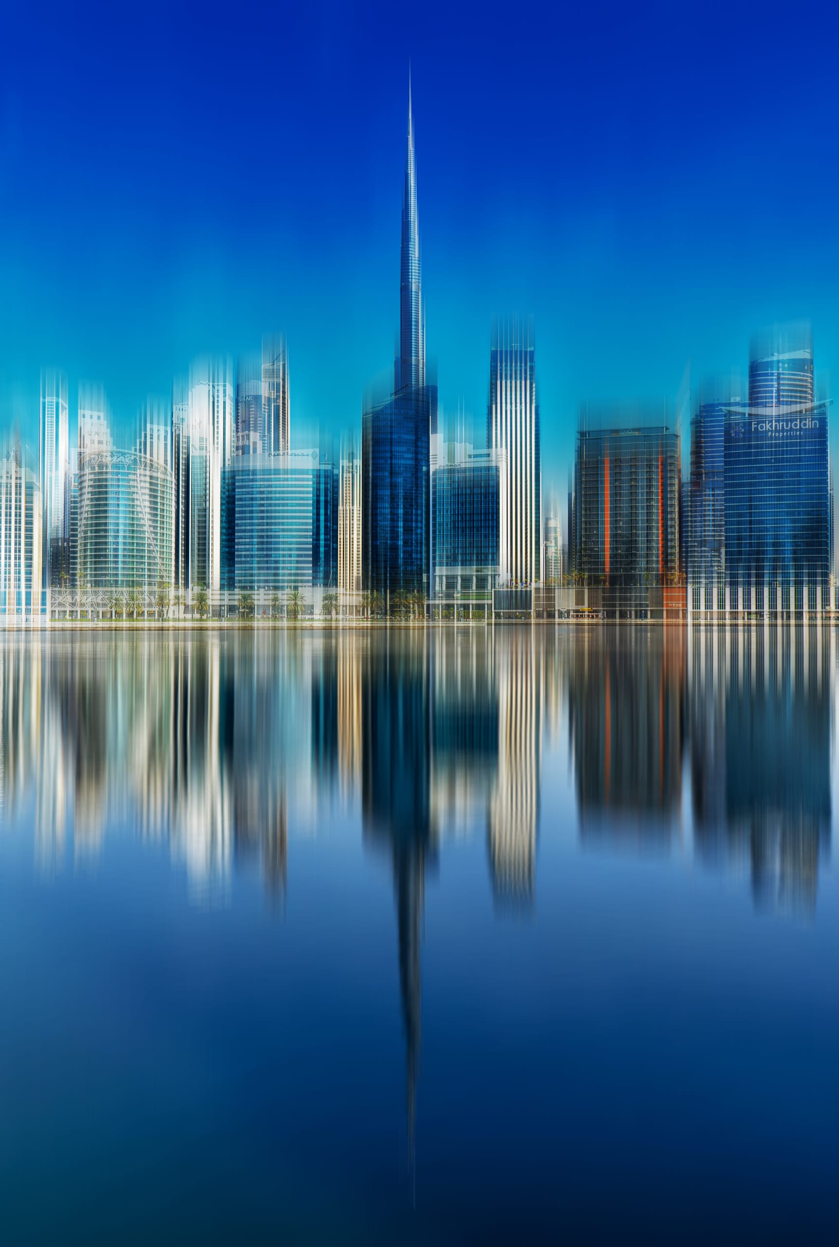 Long-exposure photograph of modern skyscrapers and their reflections mirrored across calm water, rendered with vertical motion blur and blue color cast.