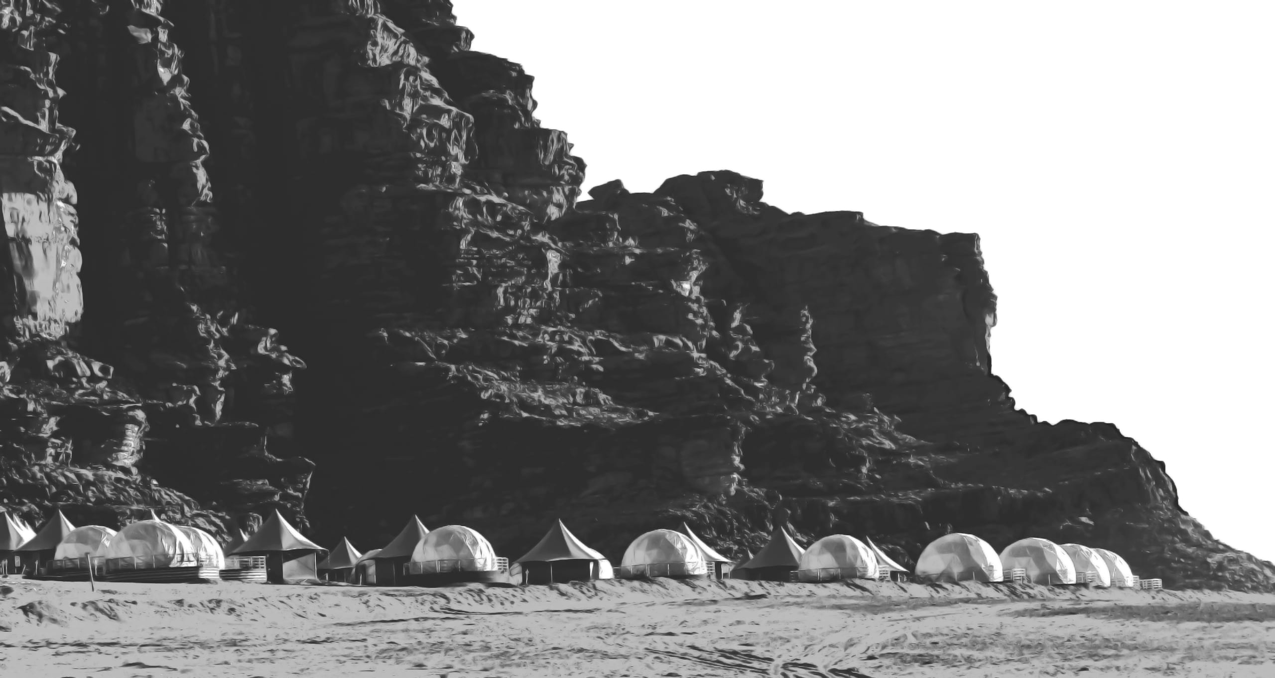 Monochrome landscape photograph showing a line of dome tents and angular shelters deployed along the base of a massive, craggy rock cliff.