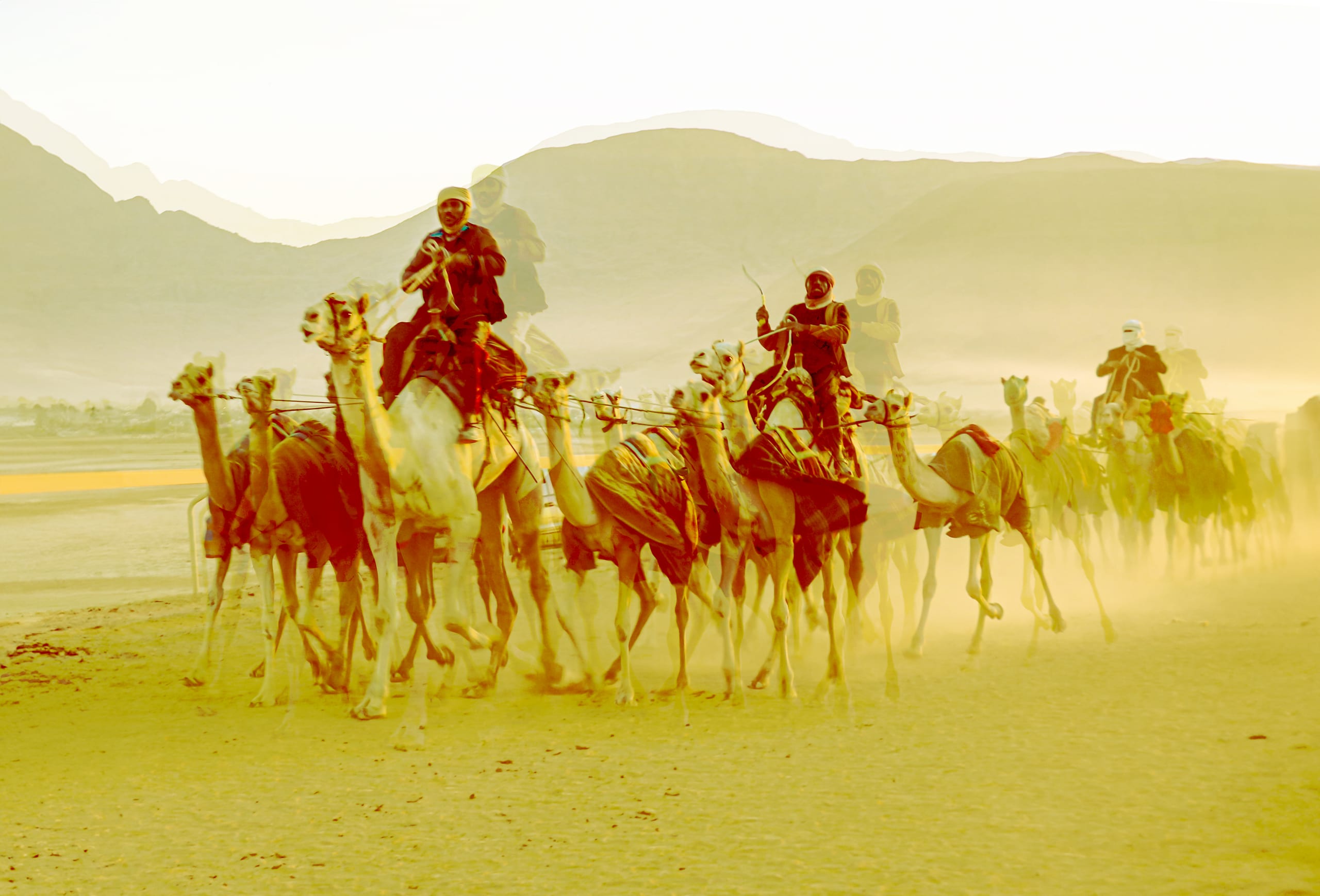 A group of riders on camels moving across a sandy landscape in a line, rendered in warm golden tones with visible motion blur and dust kicked up from the ground.