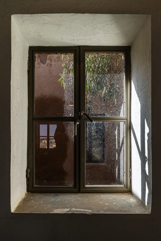 Interior view of a double-paned window set inside a thick white plaster wall with angled sunlight casting shadows on the right reveal.