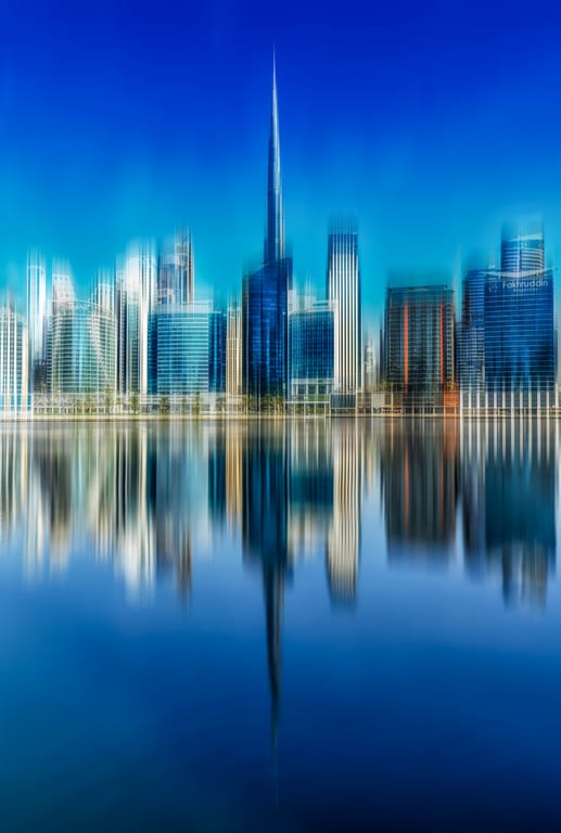 Architectural skyline reflection on water with vertical motion blur creating vertical streaks of blue and white tones.