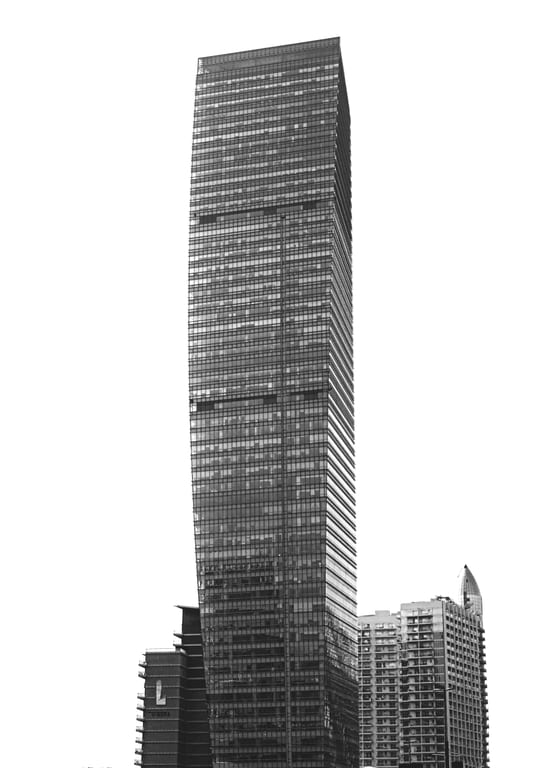 Monochrome architectural photograph of a tall, modern skyscraper featuring uniform rows of glass windows, set against a completely white sky with smaller buildings visible at its base.