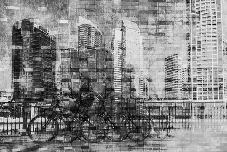 A black-and-white multiple exposure photograph showing a cyclist in motion against a backdrop of towering high-rise buildings and overlapping architectural grids.