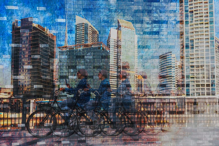 Multi-exposure photograph of a cyclist riding past modern skyscrapers, with layered reflections and overlapping silhouettes creating an abstract urban landscape.